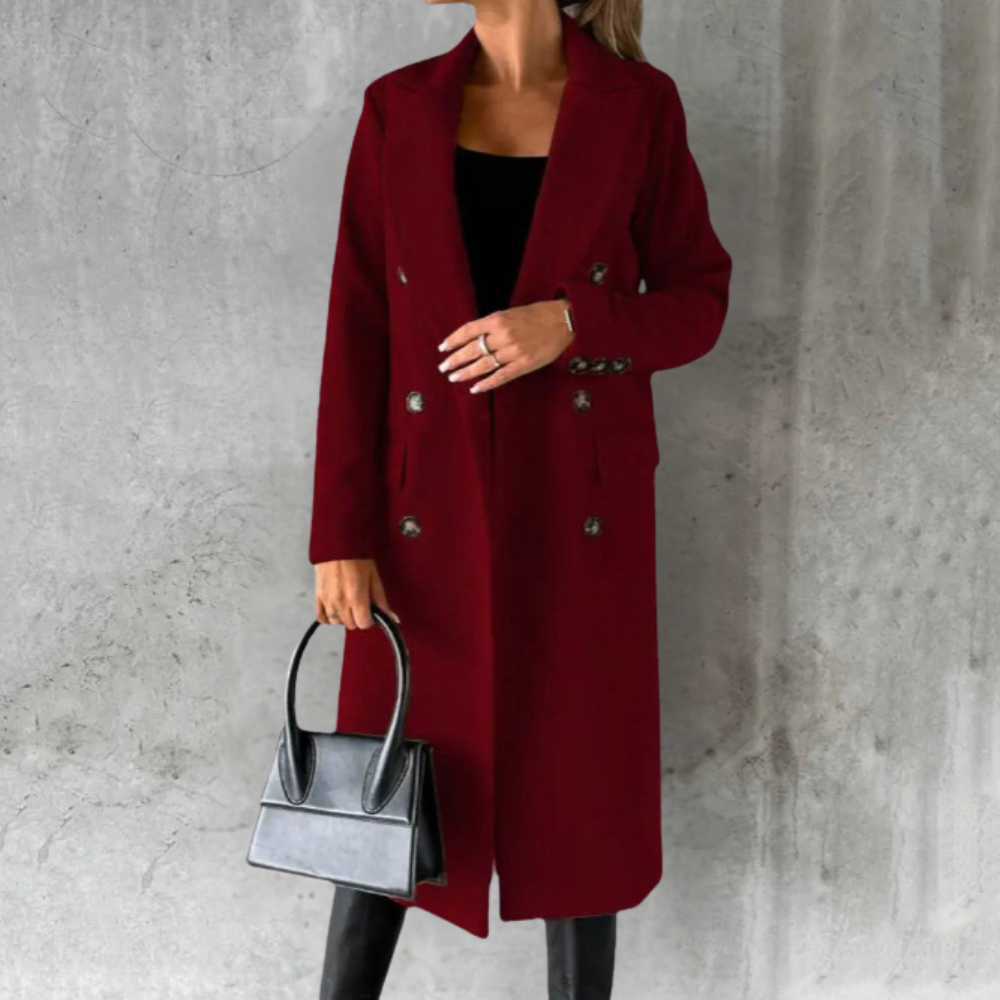 Women's long wine red double-breasted trench coat styled over a dark top and black trousers, carrying a black handbag.