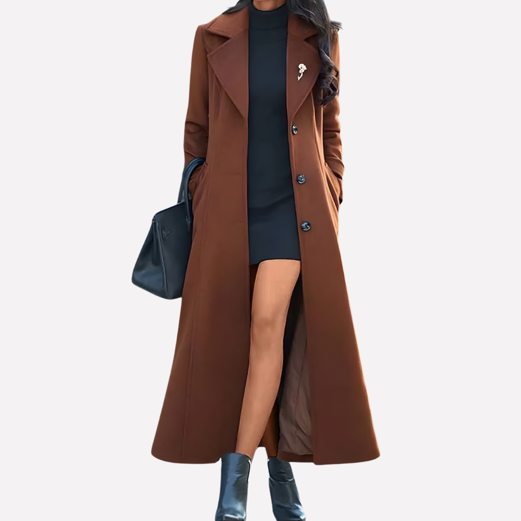 Women's long brown double-breasted trench coat styled over a dark blue dress and tall blue boots.